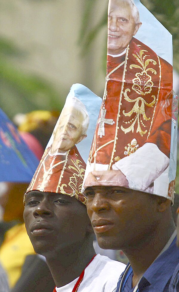 Zwei Pilger in Luanda tragen einen Sonnenschutz mit Papst Benedikt XVI. aufgedruckt.
