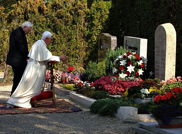 Papst Benedikt XVI. mit seinem Bruder Georg Ratzinger am Grab seiner Eltern und seiner Schwester in Ziegetsdorf. Georg steht, der Papst kniet.