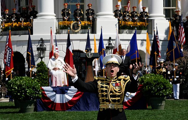 Papst Benedikt in Washington. Ein Sänger im Vordergrund. Der Papst sitz im Hintergrund auf einem Stuhl.