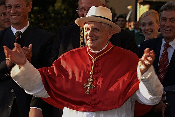 Papst Benedikt XVI. bei einer Vesper mit Ordensangehörigen und Priesteramtskandidaten in der Basilika in Altötting am 11. September 2006, während seiner Auslandsreise nach Bayern. Der Papst trägt einen Fedora-Hut, den er als Geschenk überreicht bekommen hat, er breitet die Arme aus und lacht.